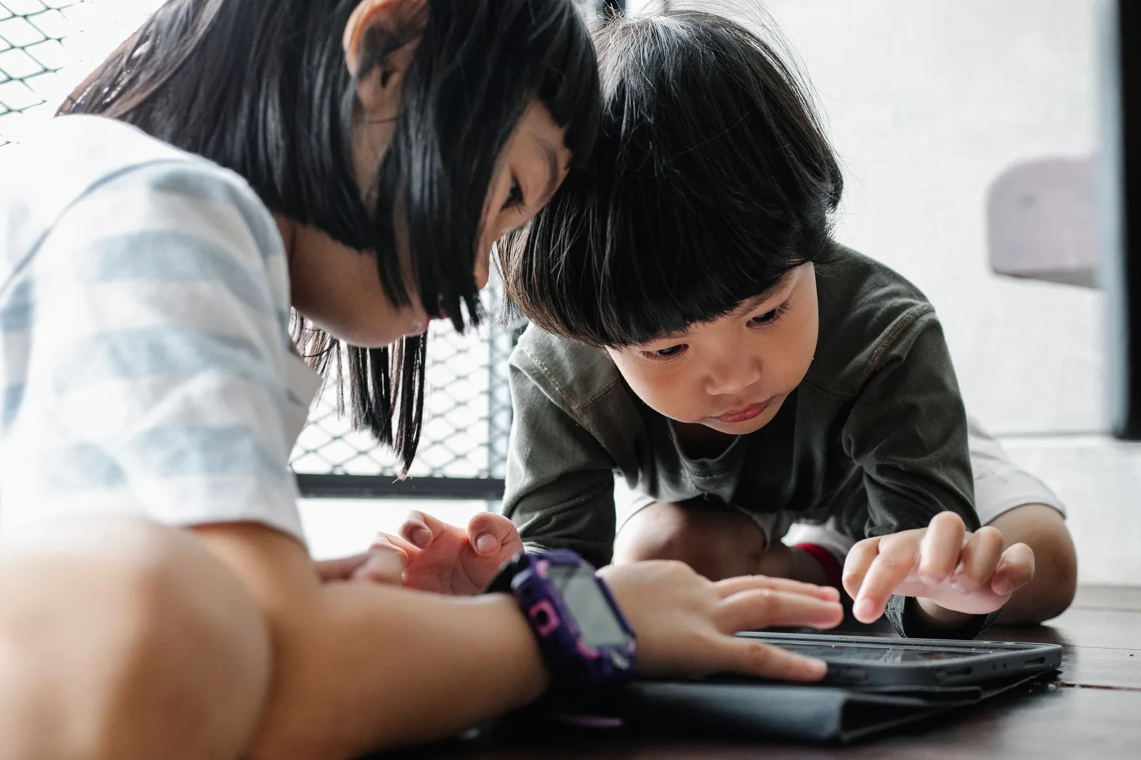 Two children sitting together looking at a tablet screen