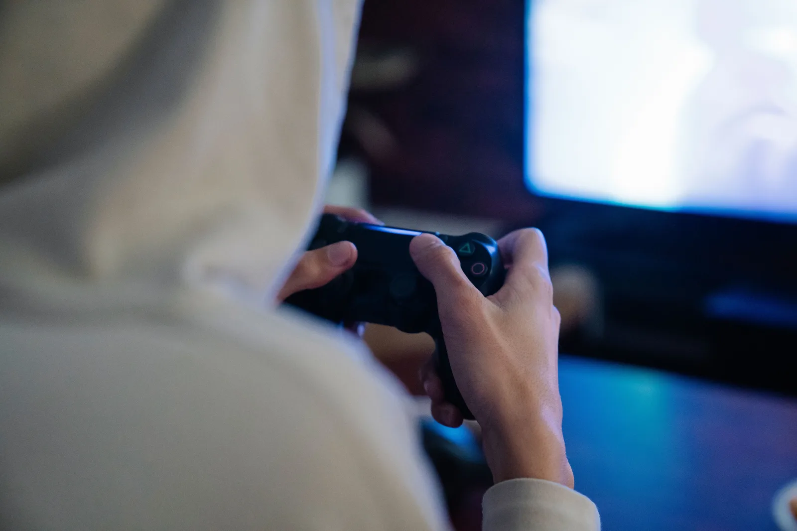 Close-up of hands holding a game controller mid-playtest, screen glowing in the background